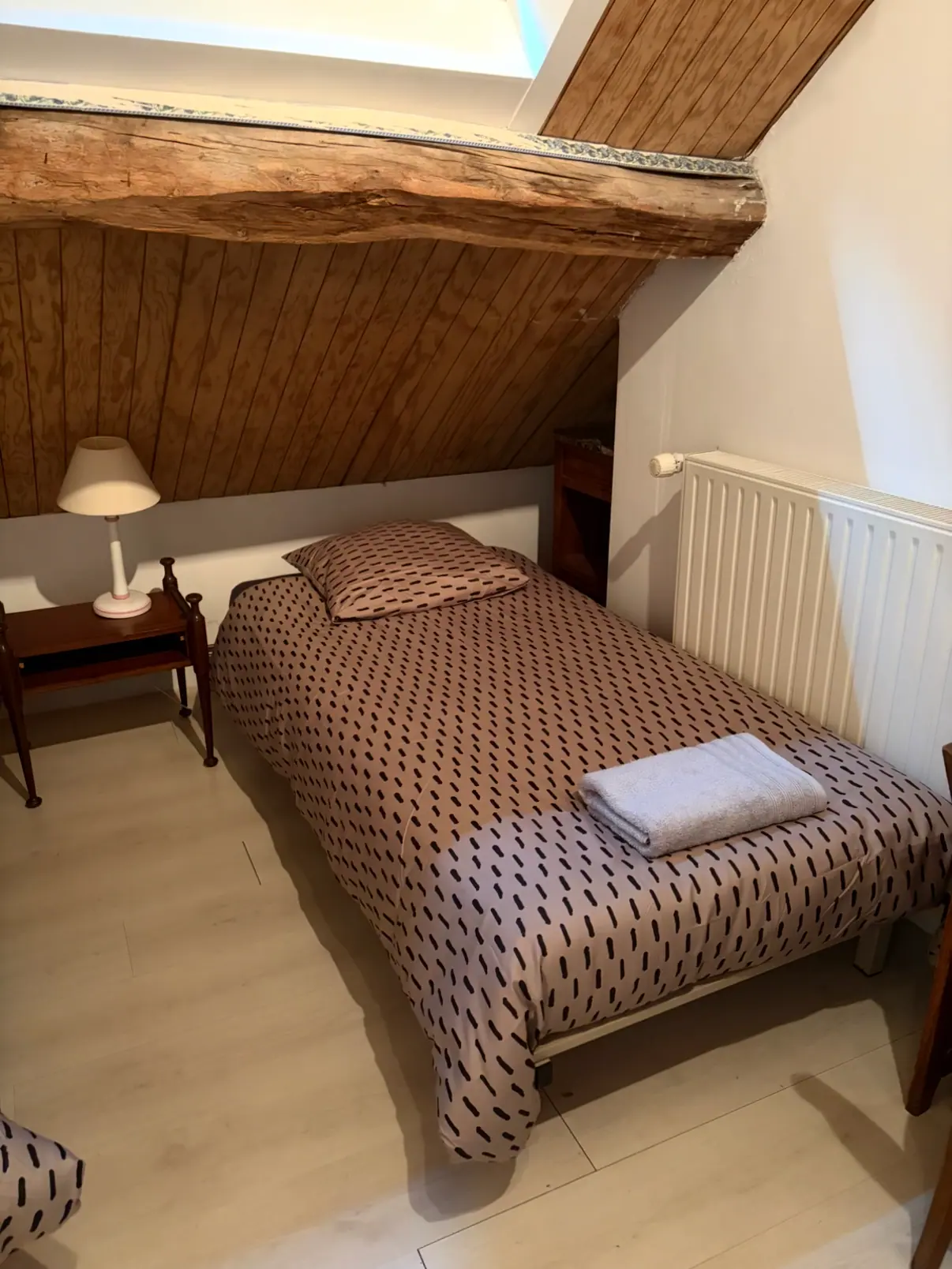 Chambre sous les combles, lit couvert d’un plaid à motifs et serviette pliée