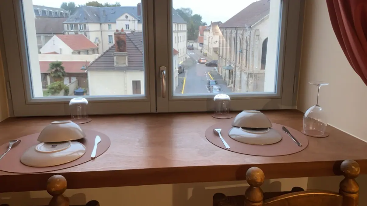 Fenêtre ouverte sur les toits et une rue d’une petite ville, comptoir en bois avec assiettes en premier plan